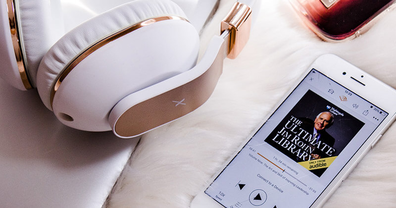 How-to-determine-audio-file-size-audiobook A pair of headphones lies next to an audiobook of The Ultimate Jim Rohn Library playing on an iPhone
